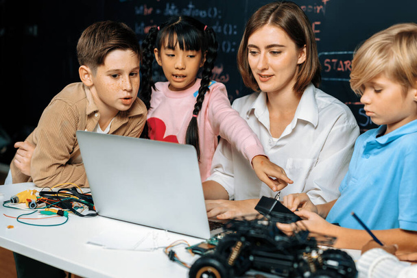 Teacher coding to demonstrate children how to code robots in the STEM class. Children fun to watch how teacher coding with confident only boy in blue shirt taking note with serious look. Erudition. - Photo, Image