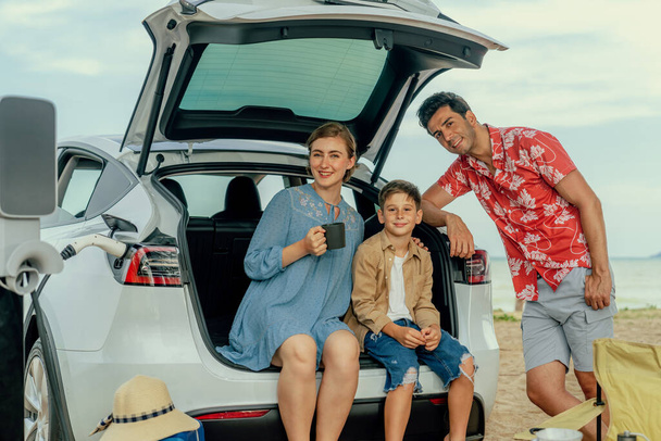 Familienurlaub Reise am Strand mit Elektroauto, glückliche Familie laden Elektroauto, genießen im Freien camping Kaffee. Seestreit und umweltfreundliches Auto für saubere Umwelt. Unvergänglich - Foto, Bild