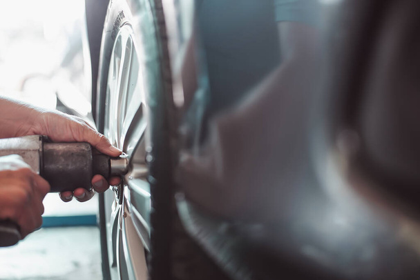 Un mecánico utiliza una llave neumática de impacto para asegurar las tuercas de la palanca en una rueda del coche, destacando la reparación profesional de automóviles. - Foto, Imagen