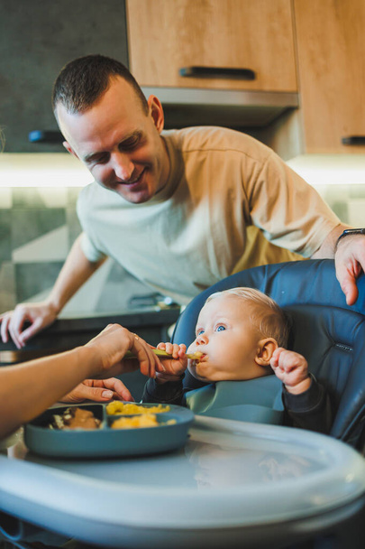 Het eerste aanvullende voedsel voor een baby. Een moeder voedt puree aan haar 6 maanden oude zoon. - Foto, afbeelding