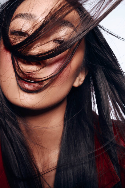 Elegante donna con lunghi capelli neri e giacca rossa che soffia capelli nel vento - Foto, immagini