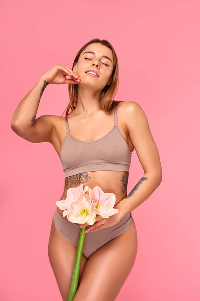 Corpo perfeito. Senhora branca magro posando com flor, mostrando suas curvas ideais, mulher atraente posando em lingerie no fundo do estúdio rosa. Cuidados com o corpo e a pele, conceito cosmetologia. - Foto, Imagem