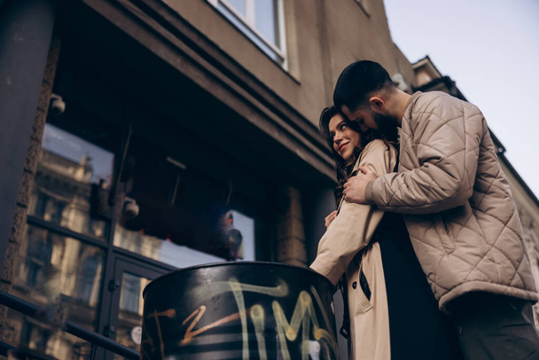 Feliz joven pareja besándose y abrazando entre la calle de la ciudad contra el fondo de los edificios. - Foto, imagen