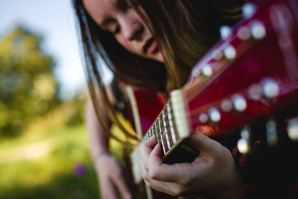 Ein Mädchen, das in das Gitarrespielen vertieft ist und die komplizierten Details ihrer Finger auf den Saiten hervorhebt, wobei ihr Gesicht im Hintergrund sanft verschwimmt. - Foto, Bild