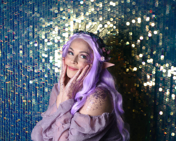  retrato de modelo femenino lindo con el pelo largo púrpura usando una corona de flores de hadas de fantasía con orejas de elfo. Aislado sobre brillante fondo de lentejuelas arco iris con purpurina. - Foto, imagen