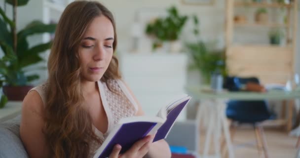 Vrouw zit op de bank thuis, diep gericht op het lezen van een boek voor studie - Video