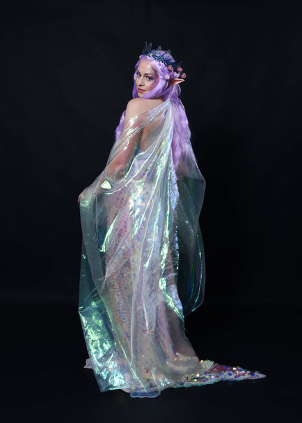 Retrato de cuerpo entero de la hermosa modelo femenina con el pelo largo de color púrpura con orejas de elfo, una corona de hadas de fantasía y vestido de lentejuelas arco iris brillante. alejándose, vista trasera, estudio oscuro aislado  - Foto, Imagen