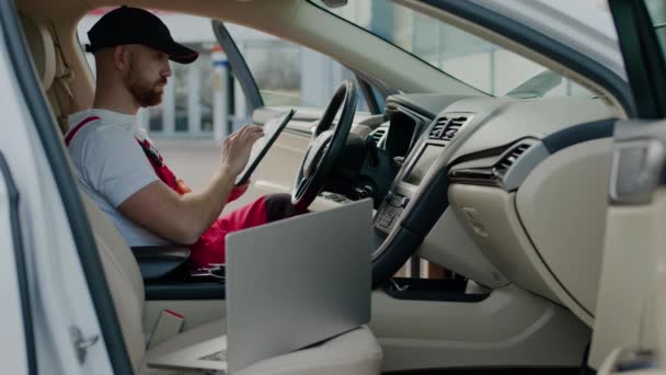 Καθισμένος στο εσωτερικό lap-top αυτοκινήτων τεχνικός διεξάγει διαγνωστικές δοκιμές οχημάτων δυσλειτουργία αυτόματη υπηρεσία. Μέσα ο κύριος μηχανικός οχημάτων χρησιμοποιεί το lap-top εντοπίζει το αυτόματο κέντρο υπηρεσιών αυτοκινήτων - Πλάνα, βίντεο