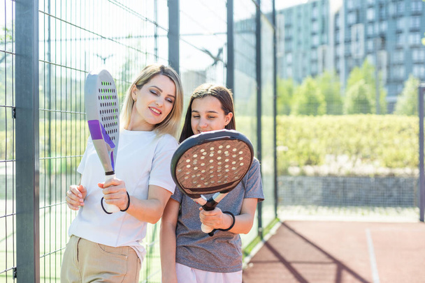 Cheerful coach teaching child to play padel tennis while both standing on tennis court. High quality photo - Photo, Image