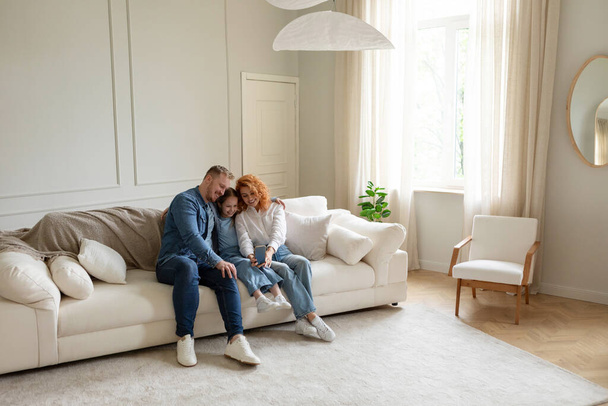 Veselí rodiče a dcera dělat selfie na mobilu, baví a odpočívá na gauči doma ve velkém obývacím pokoji, volný prostor - Fotografie, Obrázek