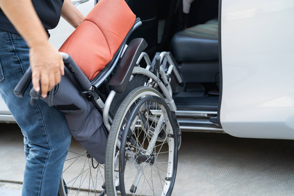 Tekerlekli sandalyedeki Asyalı engelli kadın arabasına biniyor, ulaşılabilirlik kavramı. - Fotoğraf, Görsel