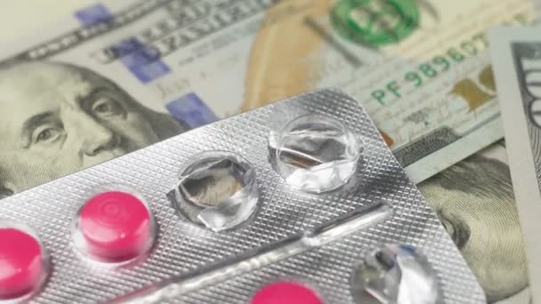 100ドル紙幣の上の錠剤の医薬品. 薬のブリスター ピンクのタブレット。 アメリカ合衆国の医療費。 お金と薬について. 製薬産業の再生について - 映像、動画