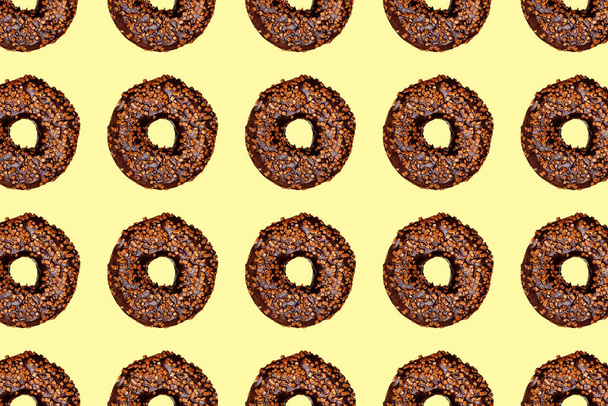 Творческий узор шоколадных пончиков с отверстиями на желтом фоне пастели. - Фото, изображение