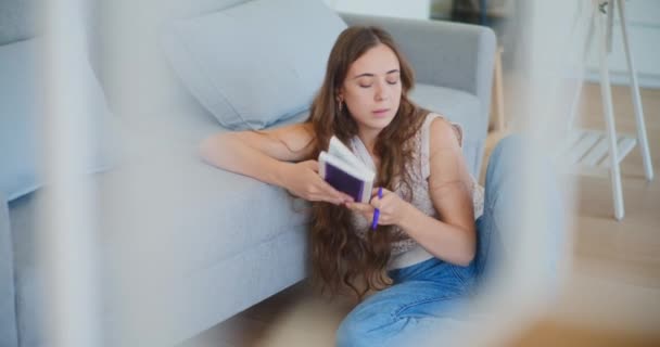 Pensive naispuolinen opiskelija sulkeminen kirja istuessaan lattialla, järkyttynyt ja ylityöllistetty - Materiaali, video