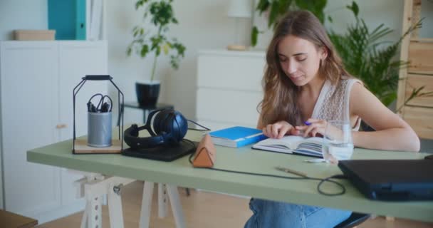 Radosna kobieta uczy się i uczy się z książki przy biurku w domu - Materiał filmowy, wideo