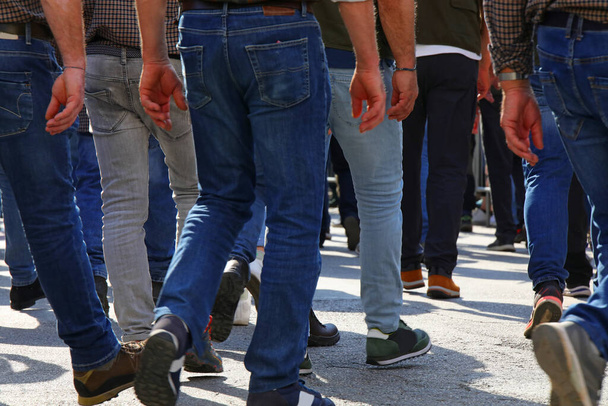 Πλήθος ανδρών περπατούν στο δρόμο με τα τζιν τους φωτογραφημένα πίσω τους. - Φωτογραφία, εικόνα