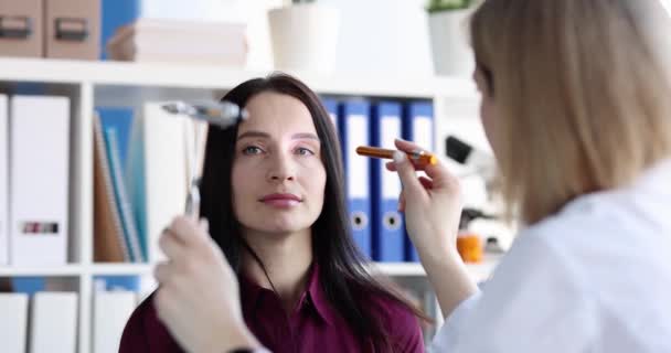 Женщина-врач проверяет глаза пациентки фонариком в медицинском кабинете. Невролог или офтальмолог проверяет концепцию зрения - Кадры, видео