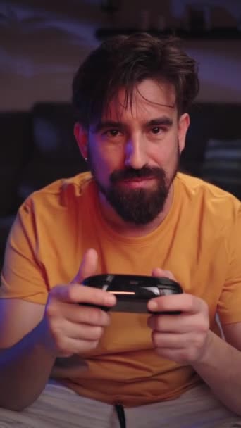 Vertikal. Kaukasischer junger Mann, der Online-Videospiele für Konsolen mit Joystick spielt, ist traurig, dass er verliert, während er nachts auf dem Fußboden des Zimmers sitzt. Chance verpasst, Meister zu werden - Filmmaterial, Video