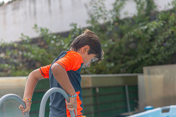 Fiatal fiú nyári fürdőruhában figyelmesen áll a medence mellett, lefelé néz. - Fotó, kép