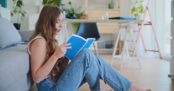 Ženské studentky sedí na podlaze u pohovky, zaměřené na čtení knihy ke zkouškám - Záběry, video