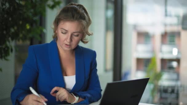 Bilgisayarda çalışan sevimli bir bayan çalışan ve ofiste otururken not defterine notlar alıyor. - Video, Çekim
