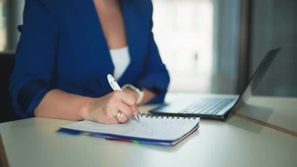 női menedzser dolgozik laptop és jegyzetfüzetbe jegyzetel, miközben ül az irodában, közelkép - Felvétel, videó
