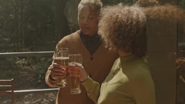 Νεαρό χαρούμενο ζευγάρι κλίνει γυαλιά σε τοστ, πίνοντας μπύρα και έχοντας μιλήσει σε υπαίθριο πάρτι στο δάσος την ηλιόλουστη μέρα του καλοκαιριού - Πλάνα, βίντεο