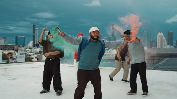 Grupa wielokulturowego hipstera grającego w kolorowe flary na dachu. Atrakcyjny uliczny tancerz trzymający kolorowy dym i wykonujący break dance przenieść się do hip-hopowej muzyki. Sport na świeżym powietrzu 2024. Endeavor. - Zdjęcie, obraz
