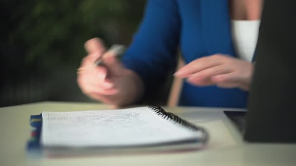 oficina en casa, mujer joven que trabaja en casa haciendo notas en un cuaderno mientras está sentado en el ordenador portátil mientras está sentado en la habitación - Imágenes, Vídeo