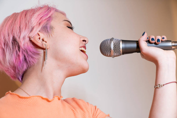 Жінка співає в мікрофон з рожевим волоссям. молода жінка співає з ентузіазмом і грайливо - Фото, зображення
