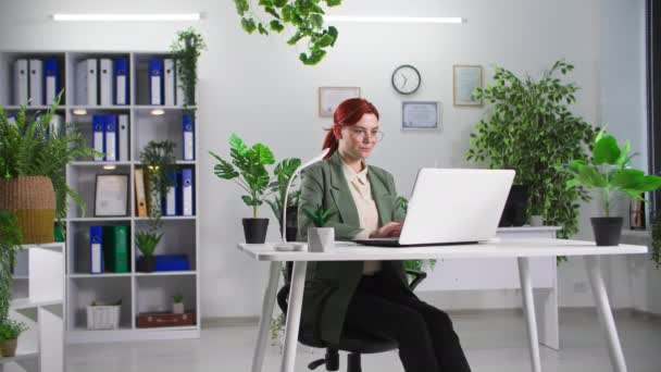 πορτρέτο νεαρής γυναίκας επιχειρηματία που εργάζεται σε φορητό υπολογιστή σε γραφείο με πράσινα φυτά - Πλάνα, βίντεο
