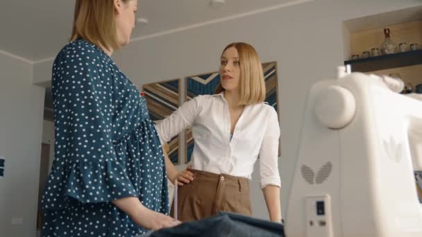 A professional fashion designer tailoring a polka dot dress on a pregnant model inside a well-lit studio space. - Footage, Video