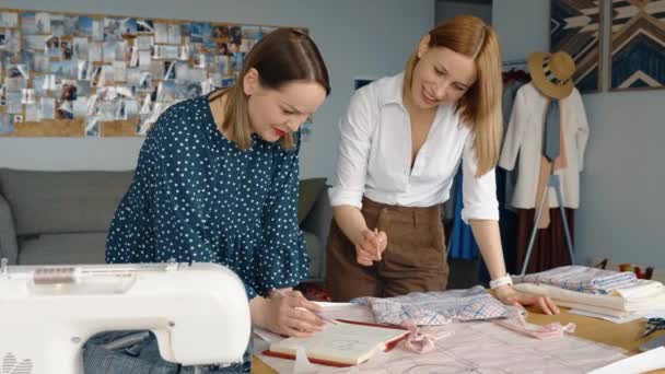 Dos diseñadores de moda enfocados trabajando juntos en un estudio, discutiendo patrones de prendas de vestir y opciones de tela. - Imágenes, Vídeo