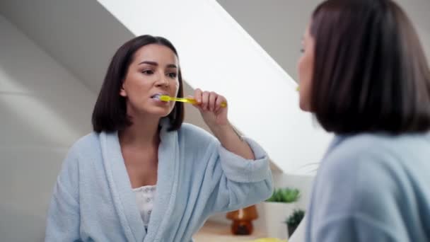 Vrolijke dame poetsen tanden met tandenborstel staan in de badkamer indoor. Brunette dame gebit routine 's avonds - Video