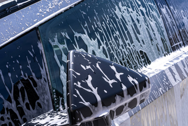 Denver, Colorado, USA-May 5, 2024-Αυτή η εικόνα συλλαμβάνει ένα κοντινό πλάνο άποψη του Tesla Cybertruck πλευρά καθρέφτη καλύπτονται σε σαπούνια suds κατά τη διάρκεια ενός πλυντηρίου αυτοκινήτων, τονίζοντας το όχημα μοναδικό γωνιακό σχεδιασμό και - Φωτογραφία, εικόνα