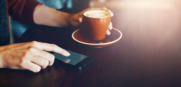 Koffieshop, telefoon en handen van persoon in restaurant voor internet, sociale media en ontspannen met een drankje. Cafetaria, lensflare en klant op smartphone met cafeïne, cappuccino en latte. - Foto, afbeelding
