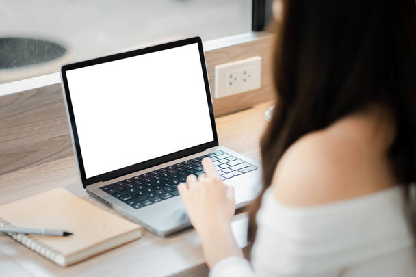 A woman is sitting at a desk with a laptop open and a notebook nearby. She is typing on the laptop, possibly working on a project or writing an email. Concept of productivity and focus - Photo, Image