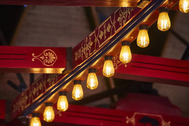 Des ampoules Edison chaudes brillent sous une balustrade riche, rouge et dorée, mêlant tradition et modernité dans un cadre intime. - Photo, image