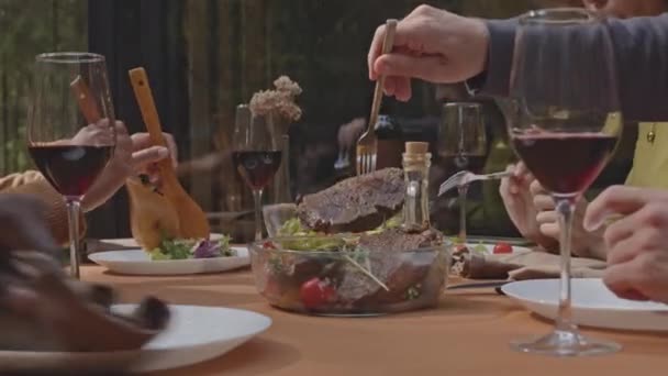 Close up view of hands of friends putting barbecue food and vegetable salad on plates while sitting at dinner table on outdoor terrace of getaway house in nature - Footage, Video