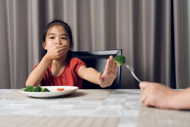 Egy aranyos kislány, aki nem hajlandó egészséges zöldséget enni. A gyerekek nem szeretnek zöldséget enni.. - Fotó, kép