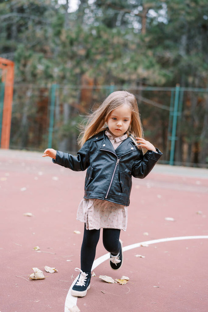 Tyttö, jolla on lentävät hiukset, kävelee leikkikentällä. Laadukas kuva - Valokuva, kuva