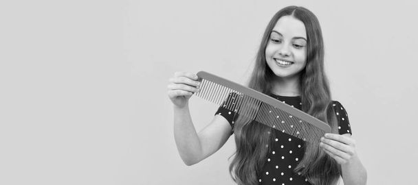 happy kid brushing long hair with comb on yellow background, haircare. Kid girl hair care, horizontal poster. Banner header with copy space - Fotoğraf, Görsel