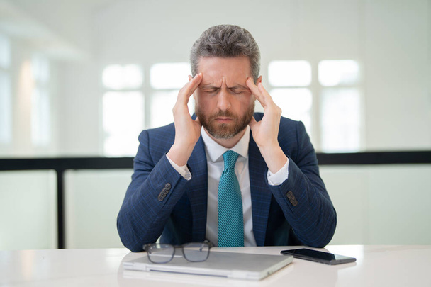 Droevige man met laptop kreeg migraine raakt haar hoofd vanwege de pijn. Man manager met sterke hoofdpijn. Overwerkte freelancer of bedrijfsleider op kantoor - Foto, afbeelding