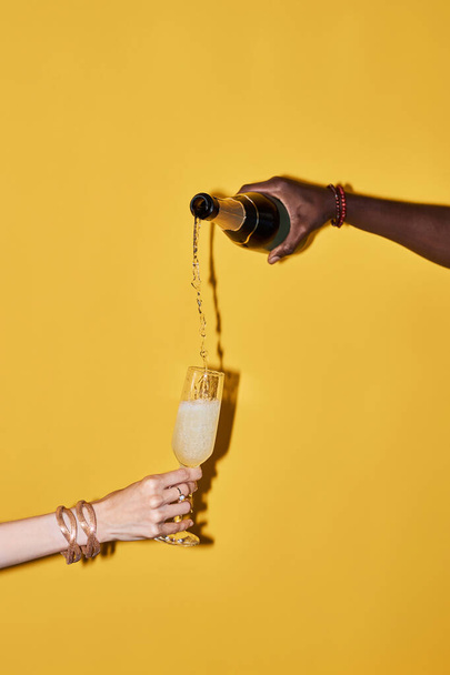 Dikey pop rengi konsepti, şampanyayı parlak sarı arka plana döken eller. - Fotoğraf, Görsel