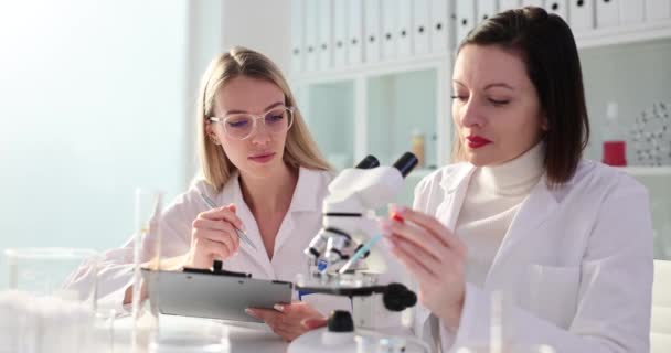 Két tudós együtt dolgozik egy laboratóriumban. Kémikusok csoportja iszik kék folyadékot mikroszkóp üvegre - Felvétel, videó