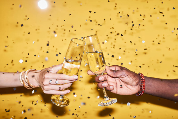 Primer plano de dos manos tintineo copas de champán contra fondo amarillo vibrante con confeti - Foto, imagen