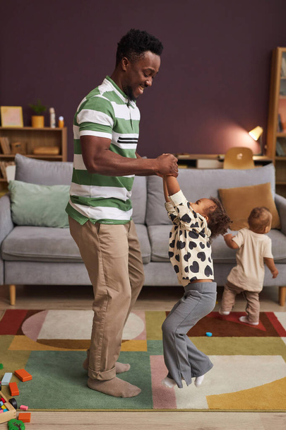 Vertical full length portrait of happy Black father dancing with cute little girl at home in living room - Photo, Image