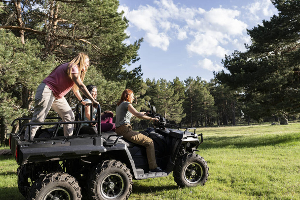 Vriendengroep die plezier hebben tijdens het rijden op een terreinwagen (ATV) door een schilderachtig dennenbos, vol gelach en avontuur. - Foto, afbeelding