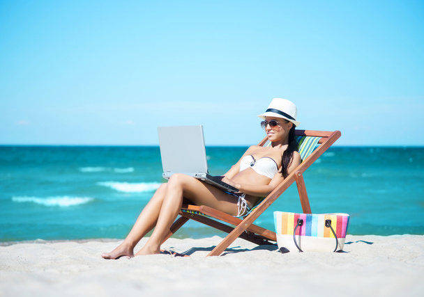Woman with laptop relaxing on beach - 写真・画像