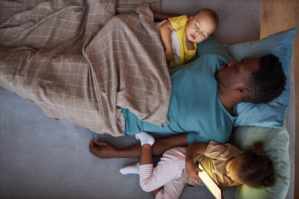 Vue du haut vers le bas de l'homme afro-américain épuisé qui couche avec deux petits enfants au moment de la sieste - Photo, image